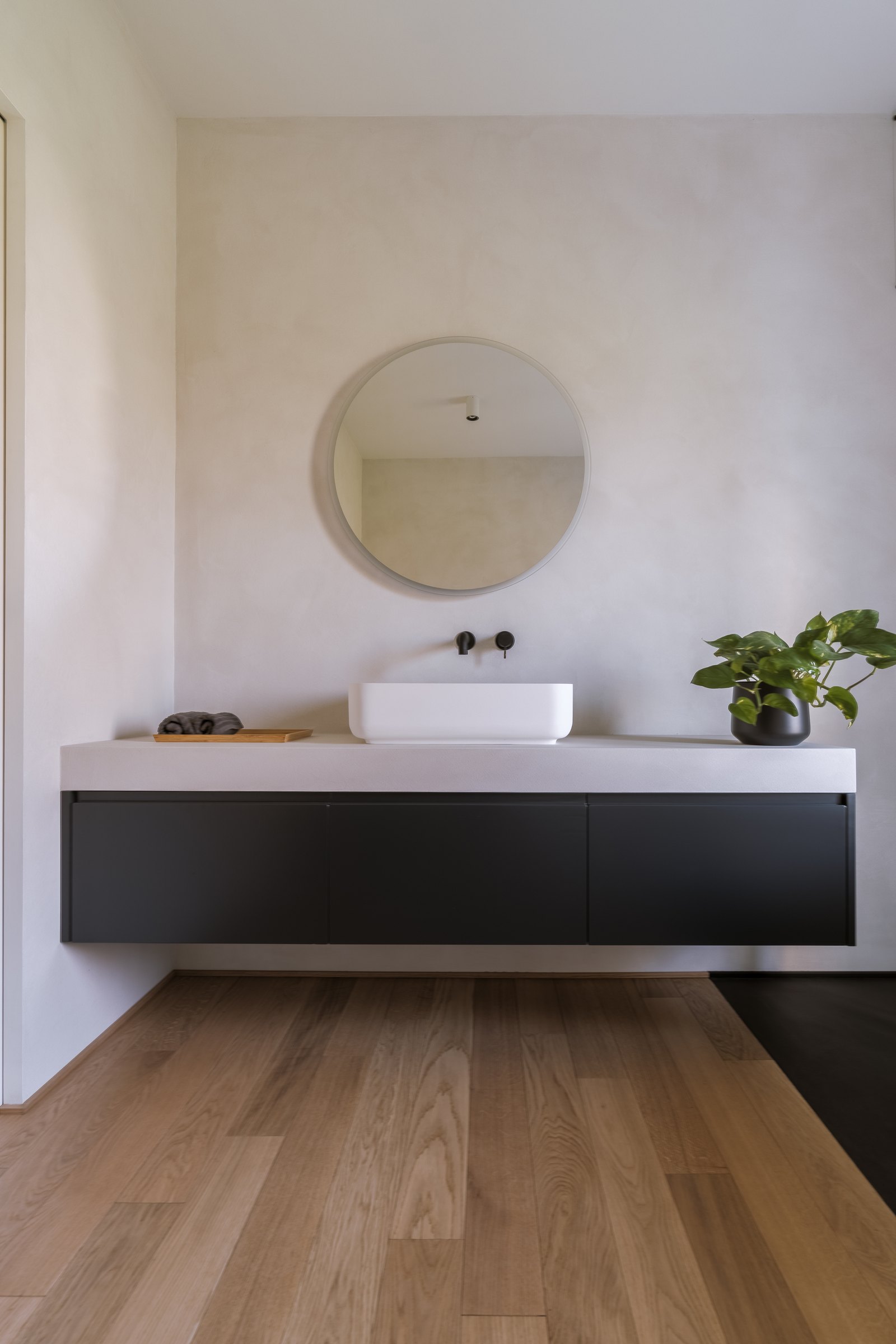 Bagno contemporaneo con lavabo d'appoggio, miscelatore a parete nero opaco e pavimento in legno