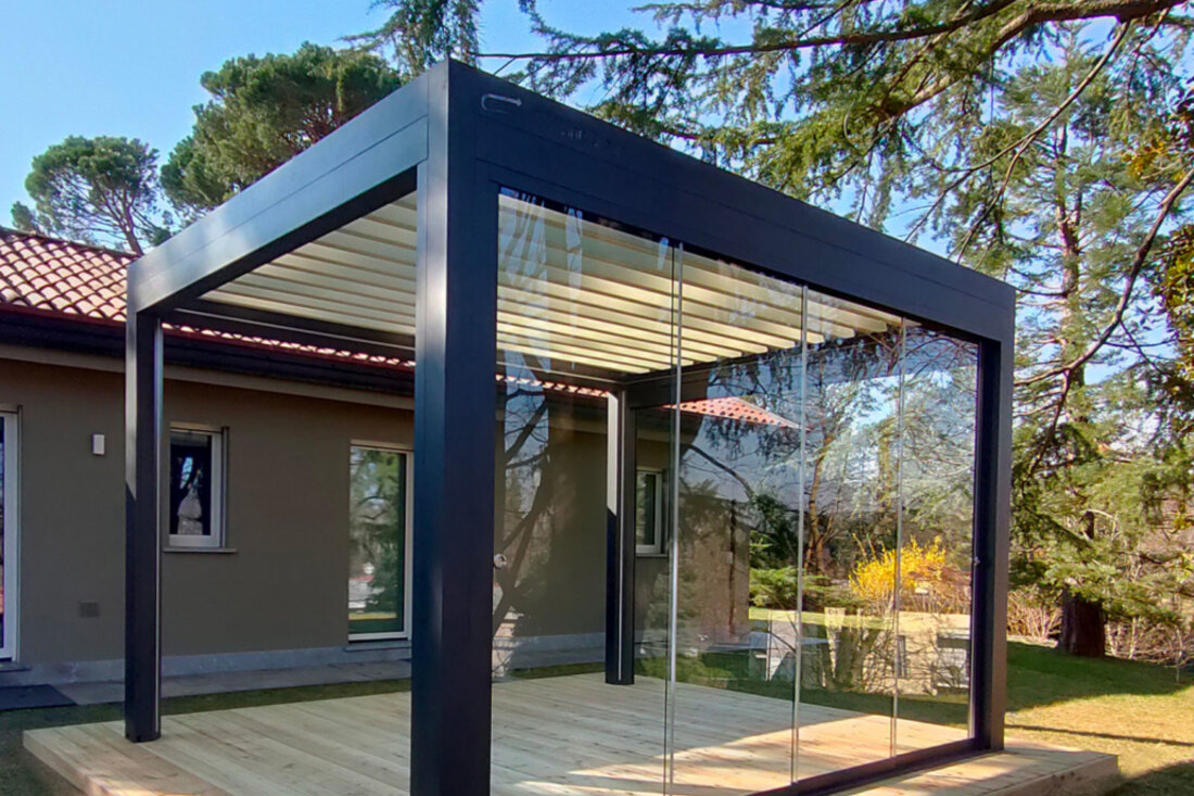 Pergola bioclimatica antracite con vetrate scorrevoli laterali su una pedana in legno